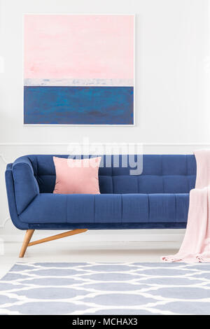 Marine blaue Couch mit rosa Kissen und Decke im Wohnzimmer Einrichtung mit gemusterten Teppich und Gemälde an der Wand Stockfoto