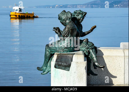 Italia, Friaul Julisch Venetien, Triest. Il Lato mare di Piazza Unità ospita La Scala Reale in cui si trova La statua in Bronzo raffigurante due Donne intente eine cucire La Bandiera italiana, l'Opera porta Il Nome di'Le Ragazze di Trieste". | Italien, Friaul Julisch Venetien, Triest. Eine Bronzestatue von Frauen nähen die italienische Flagge entlang der Uferpromenade Stockfoto