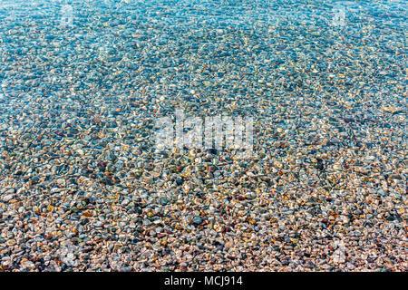 Hintergrund der farbenfrohen Meer Steine unter Wasser verschwommen. Irisierende das Sonnenlicht auf die Steine. Transparente klare Wasser des Meeres Stockfoto