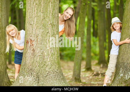 Mutter und zwei Kinder viel Spaß beim Spielen im Wald verstecken und suchen Stockfoto