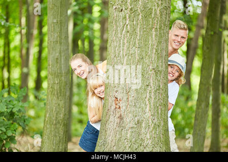 Happy Family spielt verstecken und hinter Bäumen im Wald suchen im Sommer Stockfoto