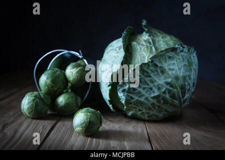 Ganze Weißkohl und Rosenkohl fallen aus dekorativen Metall Eimer auf die natürlichen hölzernen Tisch. Selektive konzentrieren. Im rustikalen Stil. Natur Stockfoto