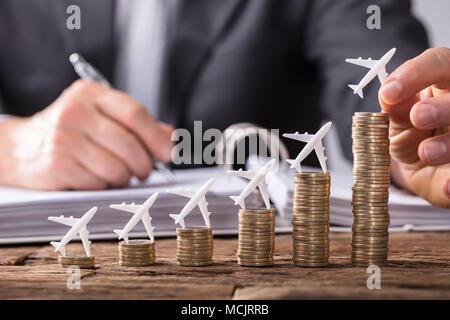 Nahaufnahme einer menschlichen Hand kleinen Flugzeug auf zunehmende Gestapelte Münzen über Holz- Schreibtisch Stockfoto