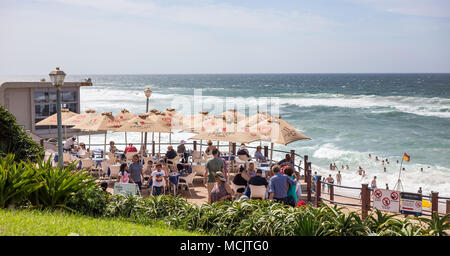 Durban, Südafrika, April 9 - 2018: Cafe entlang am Strand mit Sonnenschirmen. Die Badegäste können in das Meer im Hintergrund gesehen werden. Stockfoto