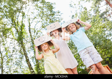 Mutter und Kinder spielen mit lustigen bemalten Kartons im Garten Stockfoto