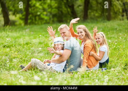 Familie mit Kindern sitzt im Gras im Garten und winkte freundlich Stockfoto