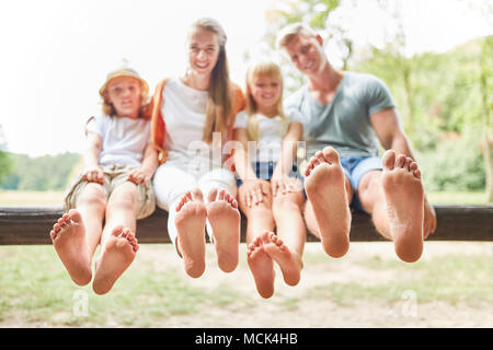 Glückliche Familie und Kinder sitzen barfuß auf einer Parkbank im Sommer Stockfoto