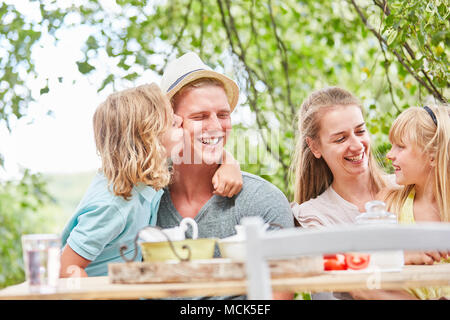 Junge gibt Vater einen Kuss auf die Wange zum Frühstück im Garten Stockfoto