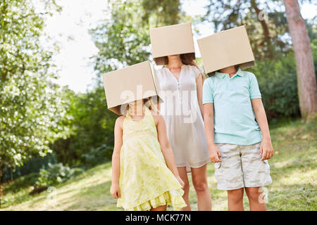 Familie mit ihren Gesichtern unter Pappkartons im Garten versteckt Stockfoto