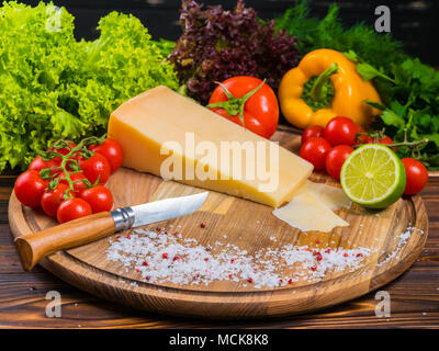 Holzbrett mit Parmesan Käse, frische Tomaten, Kopfsalat, Meersalz, Kalk, Paprika und rote bulgarischen Pfeffer. Das Messer zum Schneiden von Gemüse. Noch appetitlich Leben von Gemüse Stockfoto