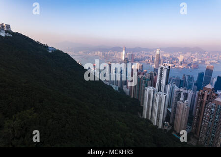 Ein Blick aus der Vogelperspektive von Hongkong zeigt die dichte Stadtlandschaft der Stadt, eingebettet zwischen einem üppigen grünen Berg und dem Hafen, was die einzigartige Geographie und Entwicklung der Stadt unterstreicht. Stockfoto