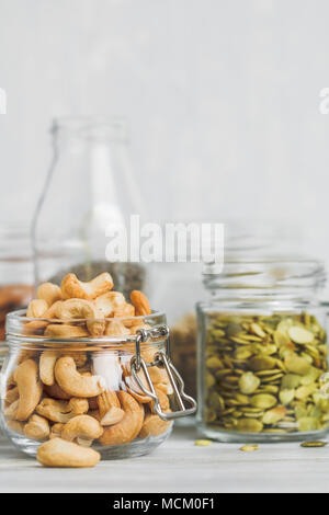 Verschiedene Nüsse und Samen, die in Gläsern über weiße Holztisch vor weißem Hintergrund. Das Konzept der vegetarischen und Bio-Lebensmittel. Einstellen der Fotos. Stockfoto