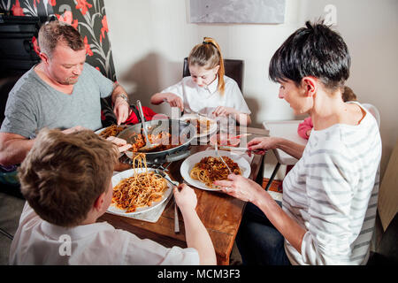 Britische Familie eine Spagetti Bolognese zusammen genießen zu Hause. Sie sitzen am Esstisch mit der Baby Mädchen in einen Babysitz. Stockfoto