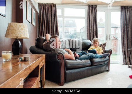 Kleiner Junge und sein Vater sind entspannende atr Home am Wochenende. Sie sitzen an einem Ende der Sofa und der kleine Junge ist mit einem digitalen Tabelle Stockfoto