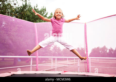 Happy kaukasische Mädchen Springen auf einem Trampolin an einem sonnigen Tag im Freien. Stockfoto