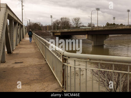 Eine Frau geht auf dem Gehweg einer Brücke an der Themse. Ungewöhnlich kühle Wetter und zwei Tage Regen, Schnee und Eisregen Stockfoto