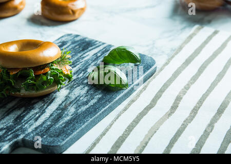 Lachs Bagel auf einem Stein schneiden Tablet mit Basilikum auf der Seite. Stockfoto