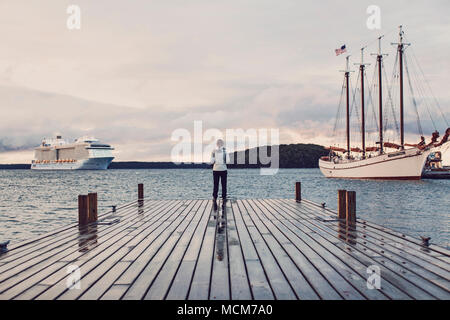 Eine Frau Uhren ein Kreuzfahrtschiff sinkt in der Nähe von einem alten Segelschiff in Bar Harbor, Maine, in der Nähe von Acadia National Park im Sommer Saison verankern. Stockfoto