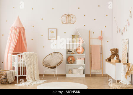 Plüschbär auf weißen Schrank in der scandi Kind Schlafzimmer Innenraum mit Krippe unter dem Vordach Stockfoto