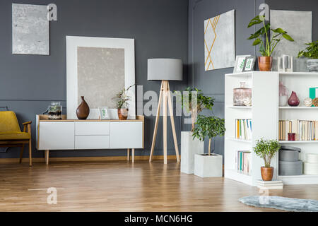 Bücher auf weißem Bücherregal und Pflanzen in Floral grau Wohnzimmer Interieur mit Gemälden an der Wand Stockfoto