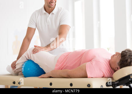 Lächelnd Therapeuten Massieren eine alte Frau mit Osteoporose über eine blaue Kugel Stockfoto