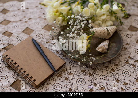 Rustikale Hochzeit Planung Konzept. Notizblock mit schwarzem Stift und kleine fresia und gypsophila Blumen bouqet auf Vintage die Platte über der Spitze der Tischplatte. Stockfoto