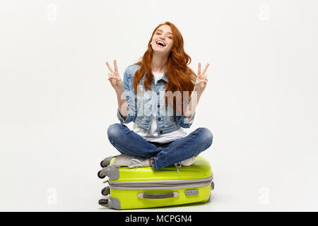 Travel Concept: junge lächelnde kaukasische Frau Standortwahl auf Koffer mit zwei Fingern. Auf weissem Hintergrund. Stockfoto