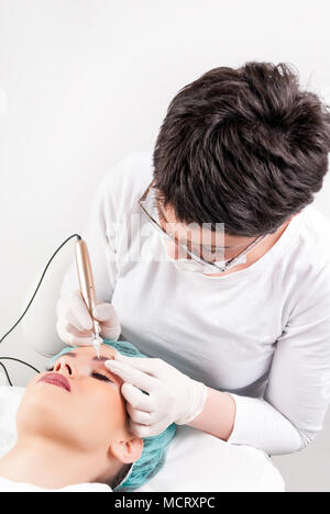 Professionelle Tätowierer permanent in Beauty Studio machen. Schöne Mädchen mit geschlossenen Augen Stockfoto