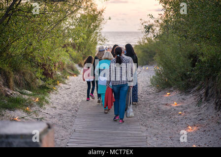 Romantische Lagerfeuer Nacht am Meer bei Sonnenuntergang. Leute versammeln um Nacht der alten Leuchten feiern. Wandern auf Holz weg am Meer Stockfoto