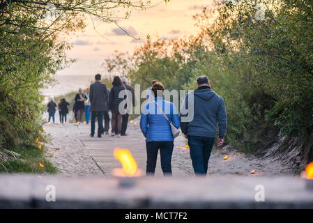 Romantische Lagerfeuer Nacht am Meer bei Sonnenuntergang. Leute versammeln um Nacht der alten Leuchten feiern. Wandern auf Holz weg am Meer Stockfoto