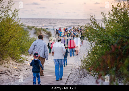 Romantische Lagerfeuer Nacht am Meer bei Sonnenuntergang. Leute versammeln um Nacht der alten Leuchten feiern. Wandern auf Holz weg am Meer Stockfoto