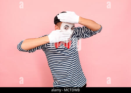 Mann im gestreiften Pullover bedeckt sein Gesicht mit den Händen. Clown, Artist, Mime. Studio shot, rosa Hintergrund Stockfoto