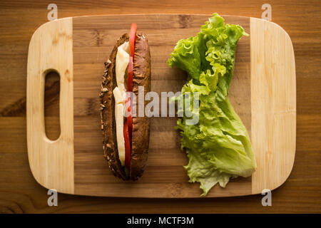 Licht Sandwich mit Käse, Tomaten und Grünen auf einer hölzernen Oberfläche. Stockfoto