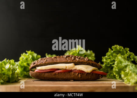 Licht Sandwich mit Käse, Tomaten und Grünen auf einer hölzernen Oberfläche. Stockfoto