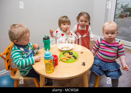 Babys und Kleinkinder mit einem Snack im Kindergarten, Großbritannien Stockfoto