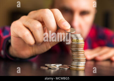 Unidentifiable man counts his coins on a table. Personal finance, finance management, thrifty or avarice concept. Stockfoto