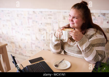 Junge erwachsene Frau Frau lächelnd, während Sie auf der Suche Kamera und Ihre morgendlichen Tasse Kaffee mit beiden Händen halten, bereit, um mit der Arbeit zu beginnen, sobald Sie Ihre tägliche Dosis Koffein hat. Stockfoto