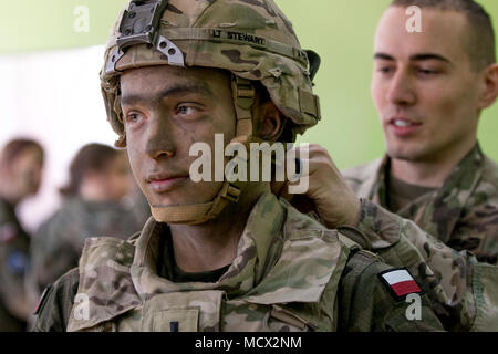 1 Leutnant Jonathan Stewart (rechts), ein Offizier der 2. Gepanzerten Brigade Combat Team zugeordnet, 1 Infanterie Division in Fort Riley, Kansas, hilft einem Kevlar Helm auf einem polnischen Cadet während eine Schule besuchen, 1. März 2018 in Rzepin, Polen passen. Soldaten aus dem 2. gepanzerte Brigade Combat Team, 1.Infanterie Division in Fort Riley, Kansas, führte ihren zweiten Besuch der Kadetten in Rzepin, dieses Mal, der militärischen Ausrüstung, damit Polnische Kadetten eine praktische Erfahrung, während der polnisch-amerikanische Allianz zu stärken. (U.S. Armee Foto von SPC. Dustin D. Biven/22 Mobile Public Affairs Abteilung) Stockfoto