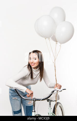 Lächelnde Frau lehnte sich auf dem Fahrrad mit Ballons isoliert auf weißem Stockfoto