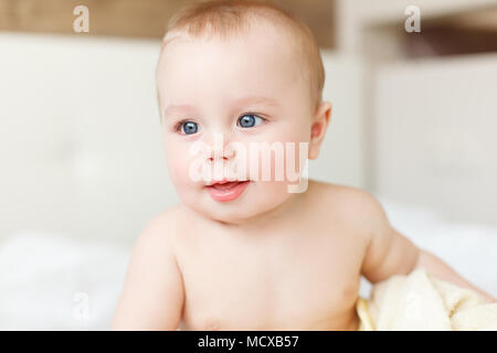 Kleine lustige baby boy lachend, wenn auf dem Bett mit Handtuch sitzen Stockfoto