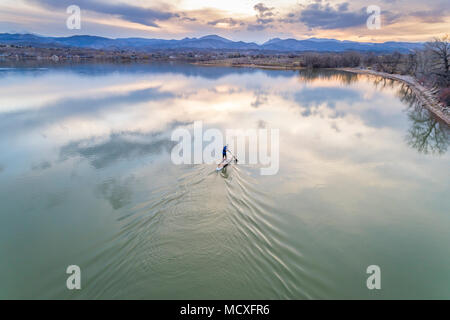 Paddeln Stand up Paddleboard bei Dämmerung auf einem ruhigen See am Fuße der Rocky Mountains in Colorado, frühen Frühling Landschaft, Luftaufnahme Stockfoto