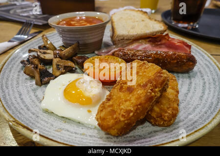 Ein Blick auf ein komplettes englisches Frühstück in einem Cafe mit Spiegelei, Würstchen, Speck, gebratene Pilze, hasb Braun und gebackene Bohnen. Stockfoto