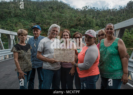 Utuado, Puerto Rico. März 13, 2018 -- Überlebenden Posieren vor der neuen Brücke und der Widmung Plakette der vorherigen zeigen. Diese Menschen unter vielen anderen Familien wurden durch den Zusammenbruch der früheren Brücke nach Hurrikan María durch die Insel am 20. September 2017 Rissen betroffen. Heute, dank der Bemühungen der staatlichen, lokalen und föderalen Agenturen, hat die Gemeinschaft eine neue Brücke. Stockfoto