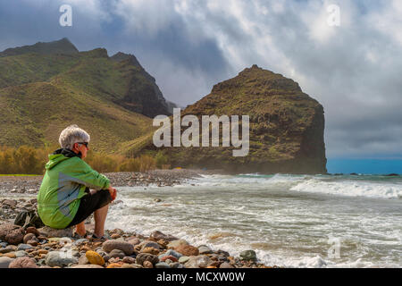 Touristische sitzt am Strand von Parque Rubén Perez vor Charco de La Aldea, Los Caserones, Gran Canaria, Spanien Stockfoto