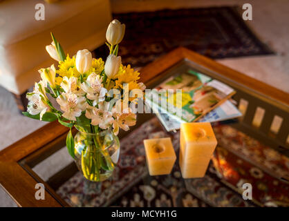 Home Inneneinrichtung in warmen Farben einstellen; Flash Schnittblumen in einem Glas, Kerzenlicht und Magazine auf ein modernes Glas Couchtisch. Die wo Stockfoto