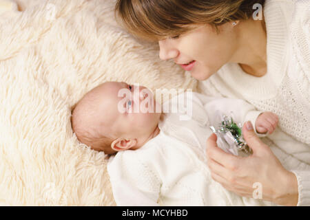 Mutter und neugeborenen Tochter liegen auf Pink Plaid. Sie sind in warmen Pullover gestrickt Weiß gekleidet. Mutter und Kind schauen sich an Stockfoto