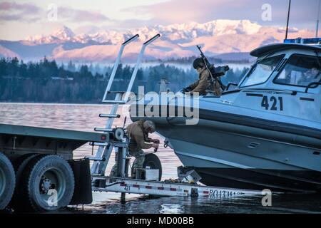 Coastal Riverine Squadron 11 ist eine Einheit der US Navy, die für die Sicherheit von Hafen und Hafen sowie für den Schutz von wertvollen Vermögenswerten verantwortlich ist. Am 6. März 2018 startete die Abteilung High Value Unit im Pazifischen Nordwesten ein 34 Fuß langes SeaArk Patrouillenboot, um die USNS Charles Drew (T-AKE-10) vom Puget Sound zur Naval Magazine Indian Island zu begleiten. Das Archivbild dokumentiert die Maßnahmen zur Gefahrenabwehr im Seeverkehr. Stockfoto