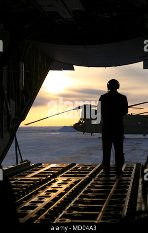 Alaska Air Guard Staff Sgt. Tyler Hoskins, ein lademeister mit den 211 Rescue Squadron, Uhren den Sonnenuntergang von der Schwanz eines HC-130J Bekämpfung König II Flugzeuge hinter einem U.S. Army Alaska CH-47 Chinook Hubschrauber in Deadhorse, Alaska, 7. März 2018. Mehr als 50 Luft und Armee Nationalgarde durchgeführten Schulungen mehrere hundert Meilen nördlich des alaskischen Küste auf dem gefrorenen Beaufort Meer. Diese Schulung ist für arktische Adler der Alaska National Guard 2018 und die U.S. Navy Ice Übung verbunden. Eine Reihe von Verteidigungsministerium Übungen leisten die teilnehmenden Kräfte die Möglichkeit in einer j zu bedienen Stockfoto