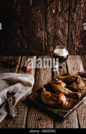 Nahaufnahme der köstliche gegrillte Hähnchenschenkel auf Holzbrett mit Glas dunkles Bier Stockfoto