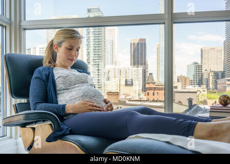 Schwangere Frau napping berühren und ihren Bauch auf Lehnstuhl Stockfoto
